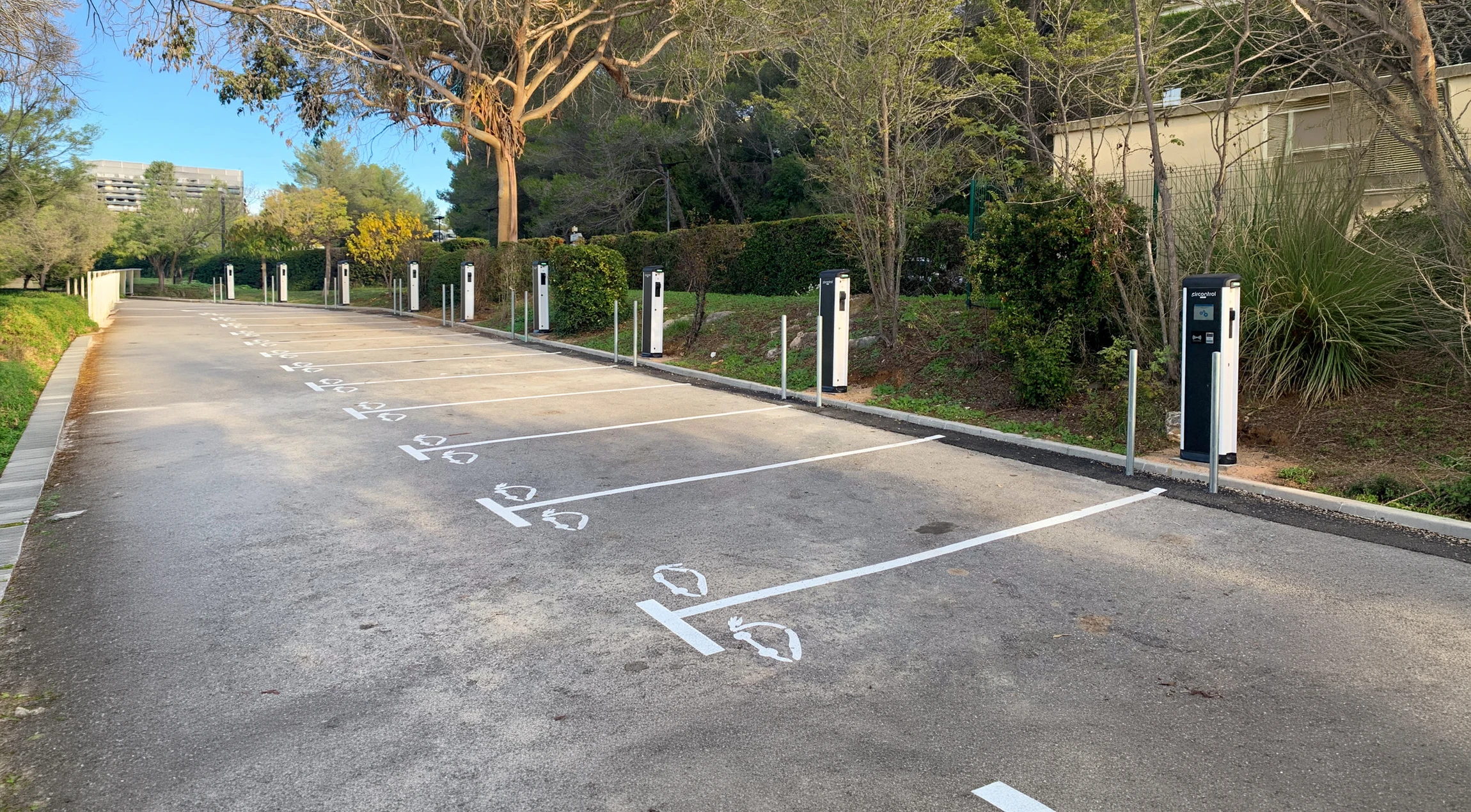 Parking ext&eacute;rieur vide &eacute;quip&eacute; de bornes de recharge pour v&eacute;hicules &eacute;lectriques, dispos&eacute;es en rang&eacute;e sur toute la longueur