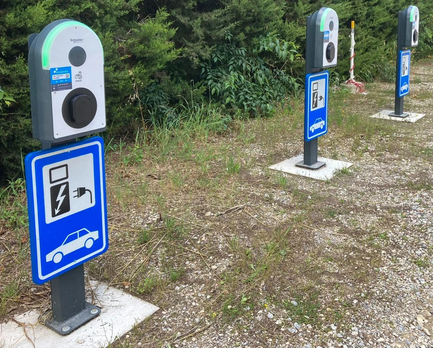 Station de recharge pour véhicules électriques en extérieur, inoccupée, sur sol de gravier avec végétation envahissante