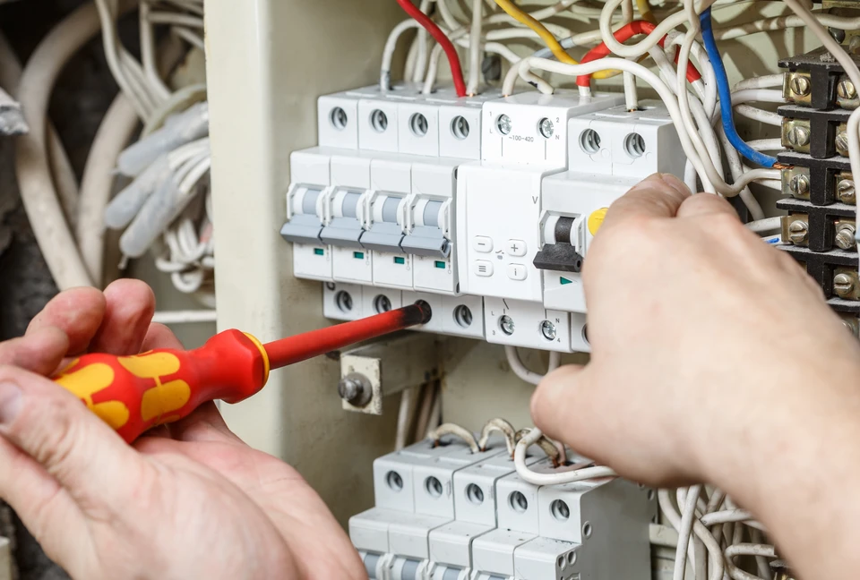 Électricien en tenue bleue effectuant des mesures électriques sur installation murale avec multimètre numérique orange