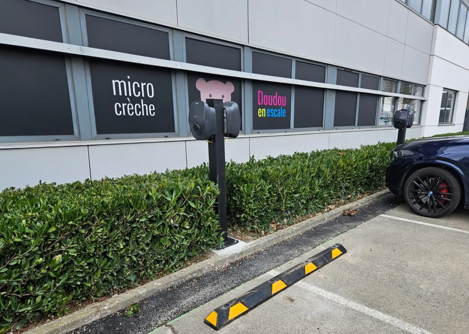 Scène extérieure urbaine avec deux véhicules électriques en charge simultanée sur une station de recharge publique
