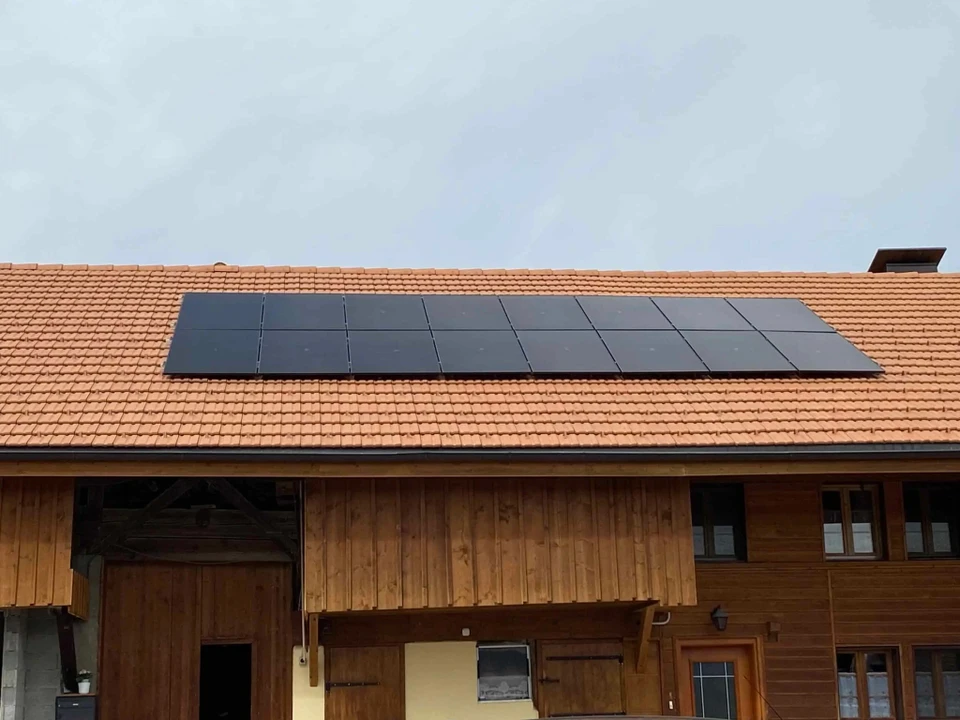 Ouvrier en tenue de sécurité haute visibilité et casque jaune installant des panneaux solaires photovoltaïques sur toiture résidentielle en bardeaux rouges, ciel bleu dégagé