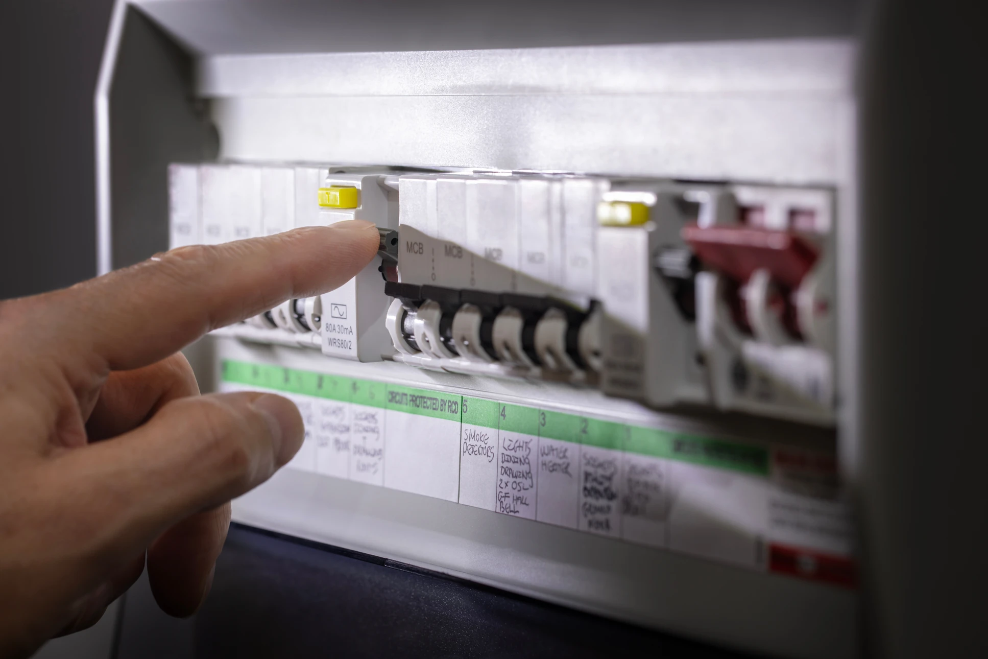 Électricien professionnel en tenue de travail avec gants blancs intervenant sur un tableau électrique industriel